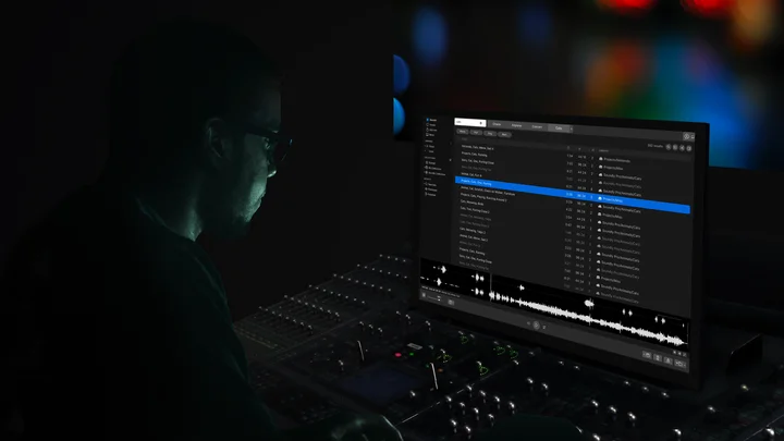 A sound designer with Soundly on a screen above a mixing console in a dark studio.