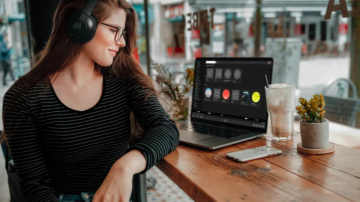 A woman wearing headphones with Soundly open on her laptop in a café.