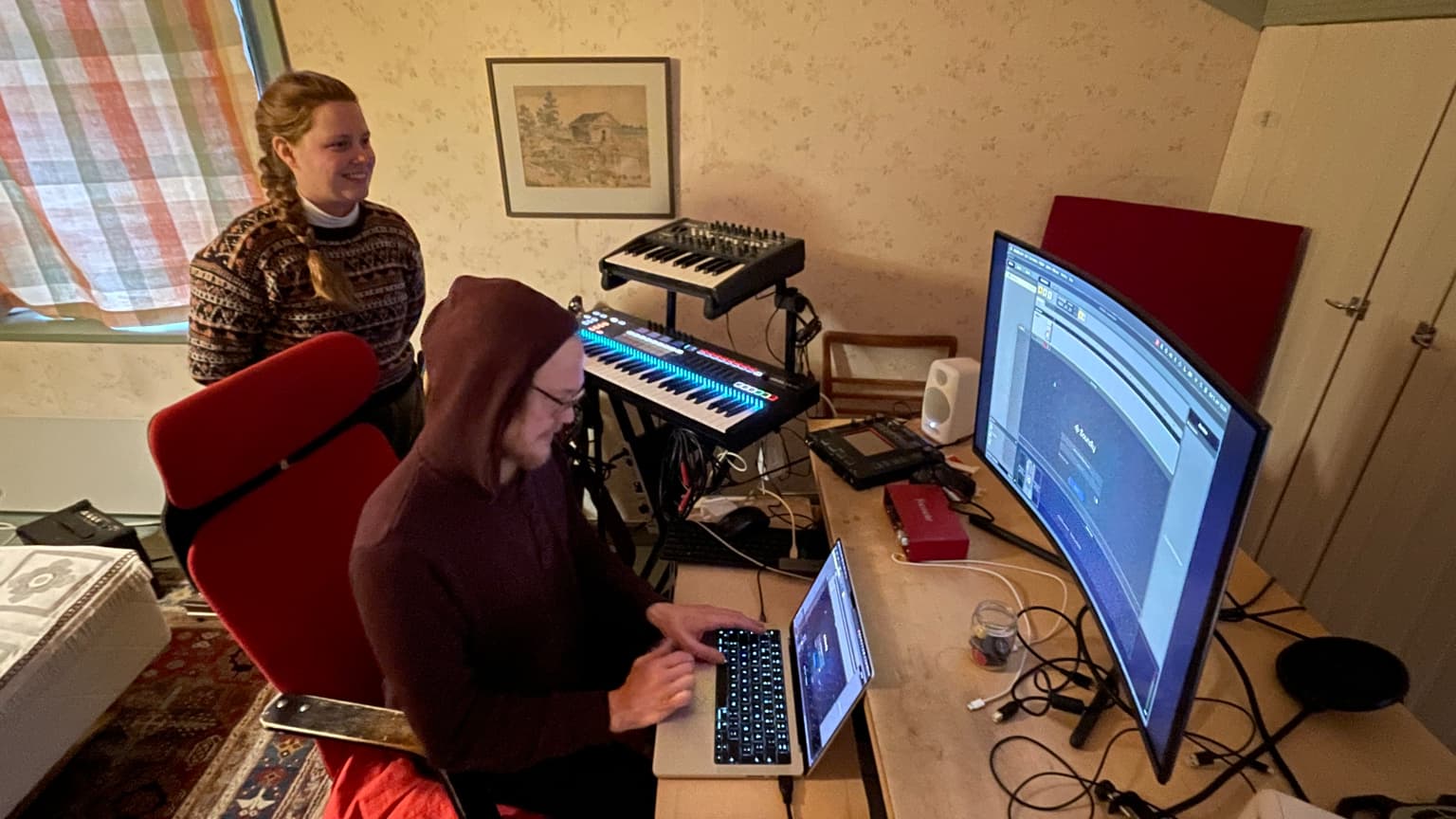 Jenni Venäläinen and Janne Storm during the Melkutus Party interview, surrounded by computers, keyboards, and audio equipment.